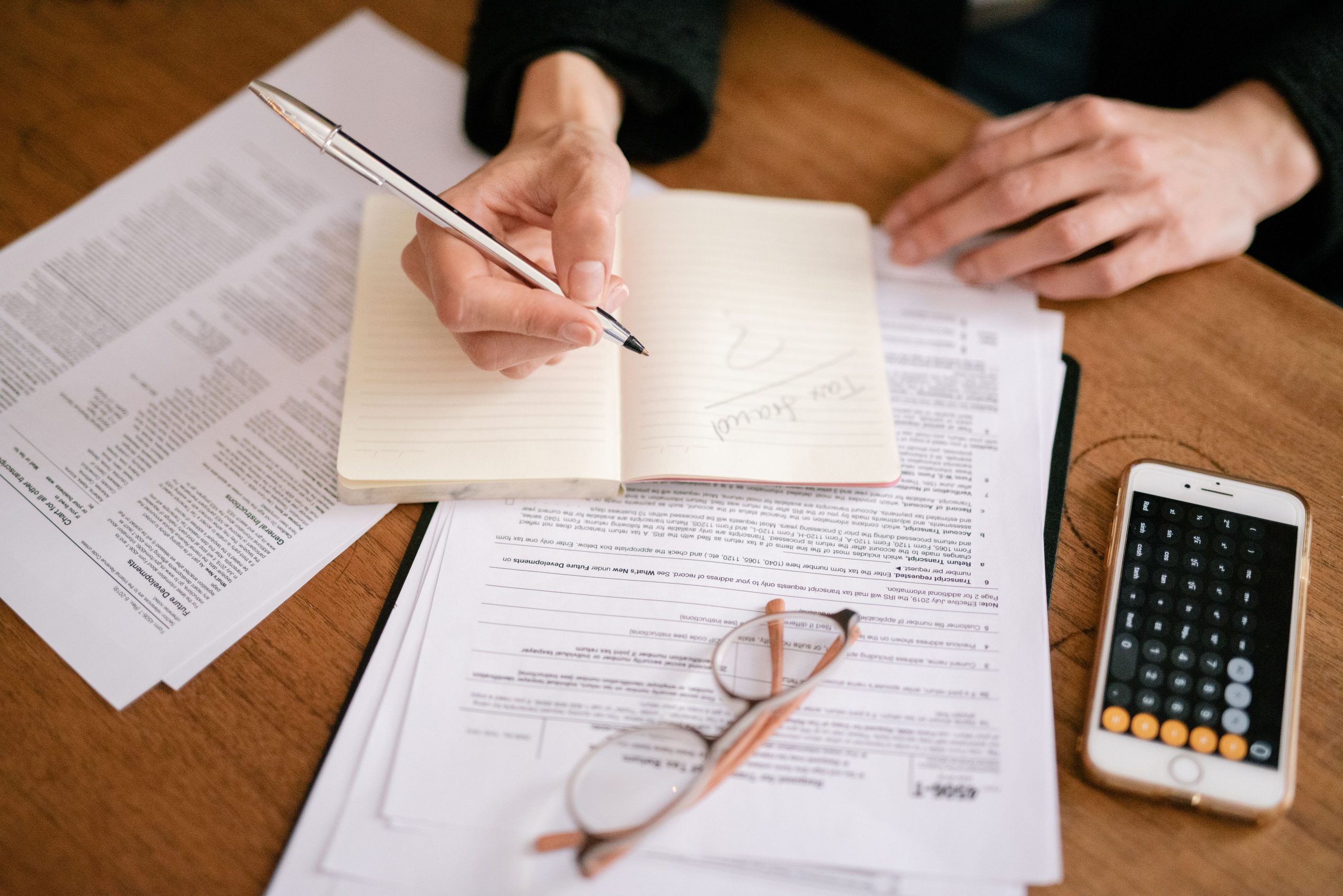 Personne écrivant dans carnet avec documents et calculatrice